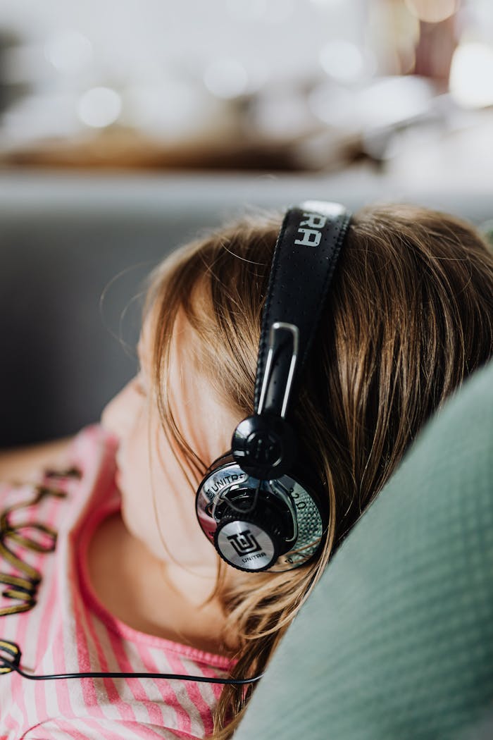 hero-gallery-03 Close-up of a young girl wearing headphones, enjoying music indoors, relaxing on a couch.