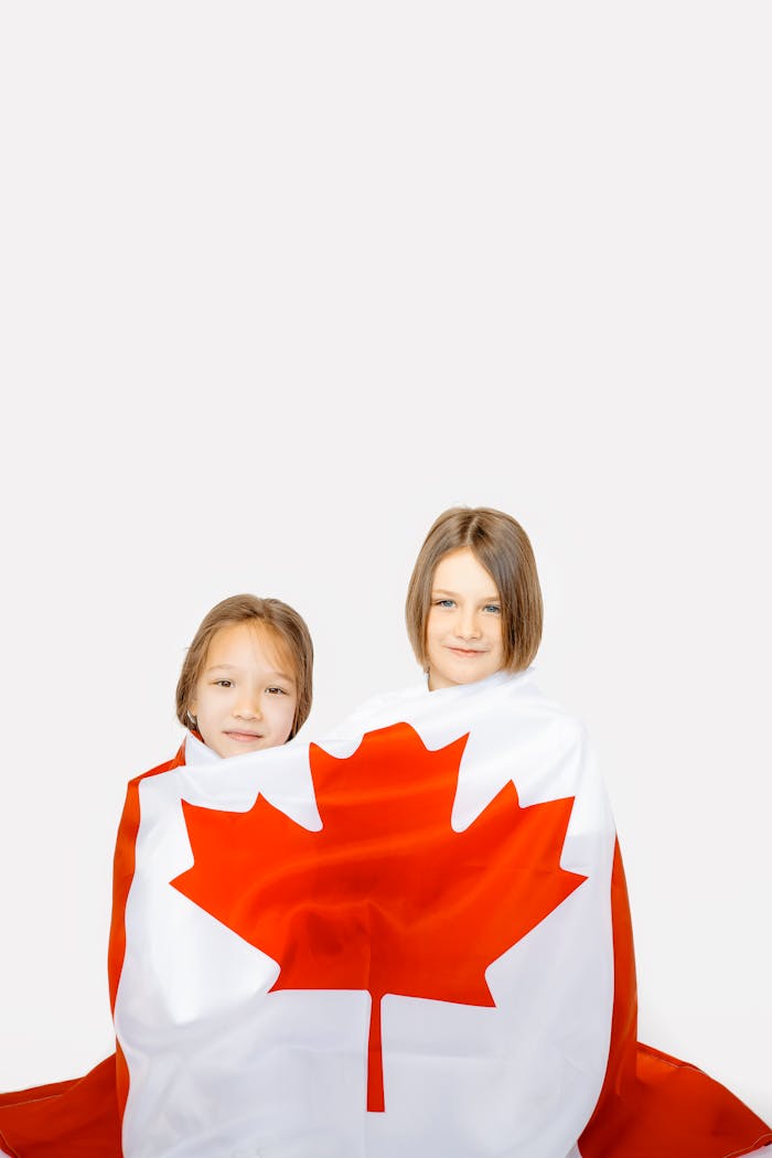 Two girls happily wrapped in a Canadian flag, symbolizing national pride.