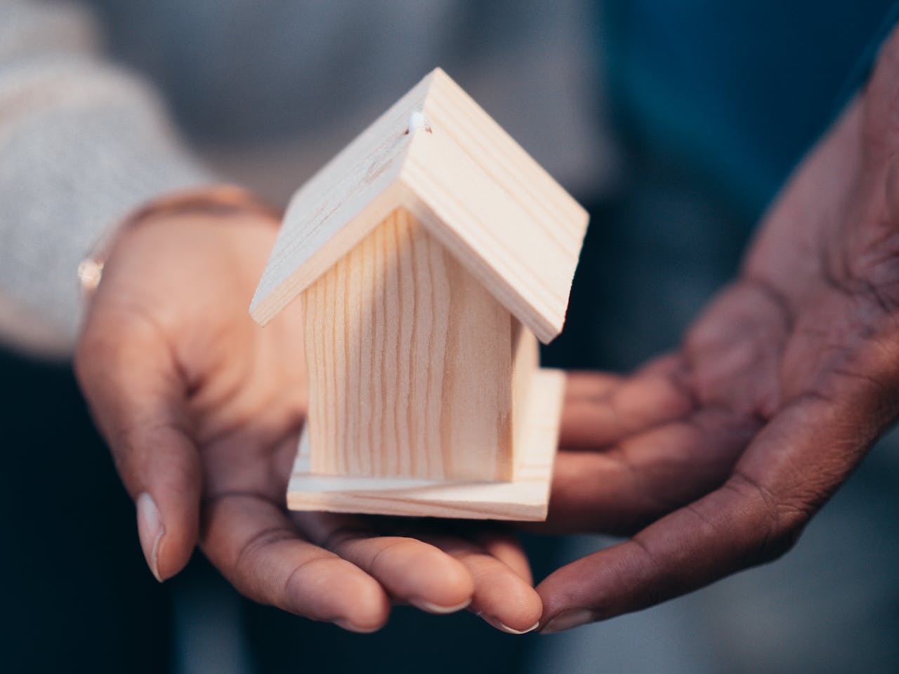 programs-02 Close-up of hands holding a wooden house model representing real estate or new home purchase.